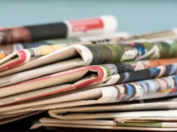 A pile of newspapers with the newspaper on top.
